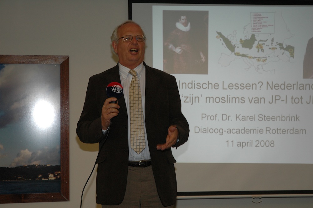 Spreker met een microfoon voor een scherm met de lezingtitel Indische Lessen? Nederland en zijn moslims