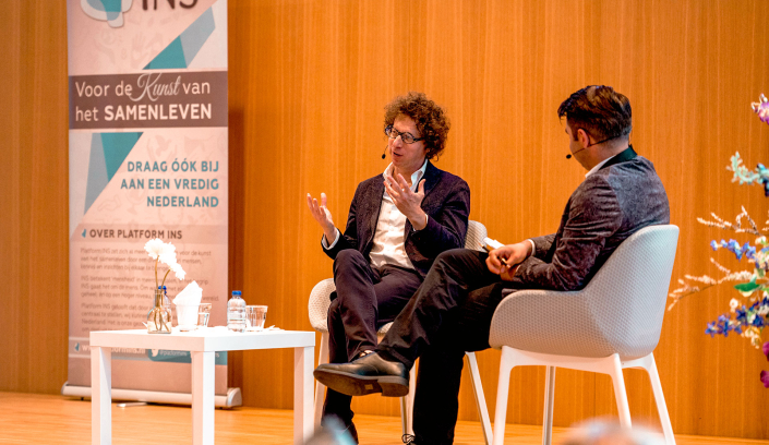 Arnon Grunberg in gesprek met een tweede spreker op het podium, naast de banner Voor de Kunst van het Samenleven